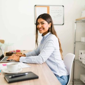 Beautiful business owner smiling and making eye contact while working at her office desk of her online startup company